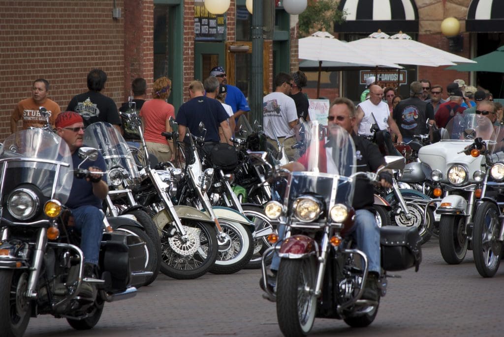 View of motorcycles parked and driving down the road during The Sturgis Motorcycle Rally